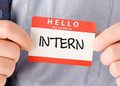 Name badge reading 'Hello, my name is INTERN' being shown by a person in a shirt and tie.