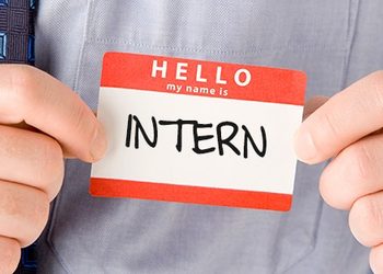 Name badge reading 'Hello, my name is INTERN' being shown by a person in a shirt and tie.