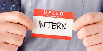 Name badge reading 'Hello, my name is INTERN' being shown by a person in a shirt and tie.