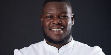 Close-up portrait of a smiling Black man in a white button-up shirt against a dark backdrop.