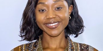 Portrait of a smiling woman with shoulder-length dark hair wearing a brown and green patterned blouse against a light background.