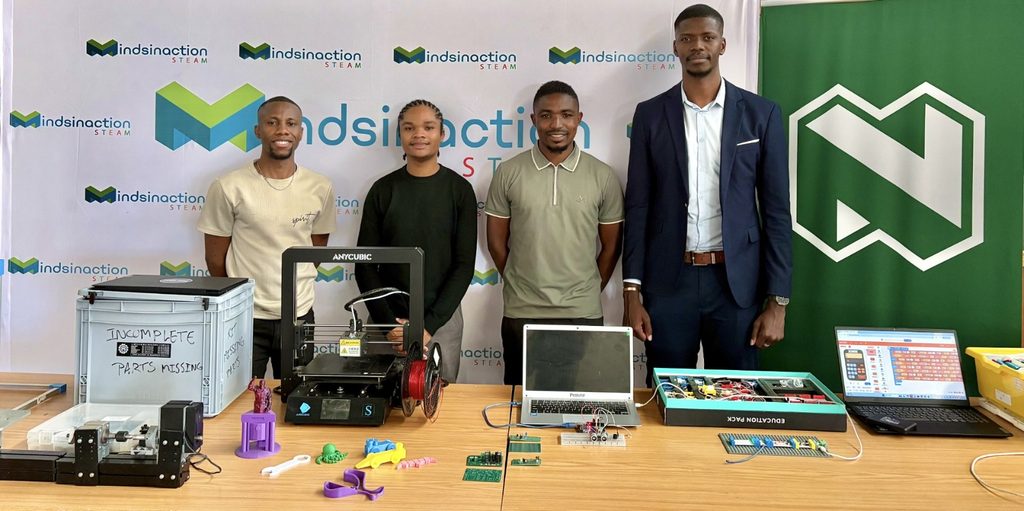 WhatsApp Image 2026-10-26 at 123543 PM - The Brief | Namibia's Leading Business & Financial News Group of four people standing behind a table with 3D printers and electronics at a tech exhibit, branded banners in the background.