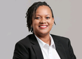 Professional headshot of a smiling woman in a black blazer and white shirt, against a light gray background.