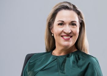Smiling woman with blonde hair wearing a green blouse against a light gray backdrop.