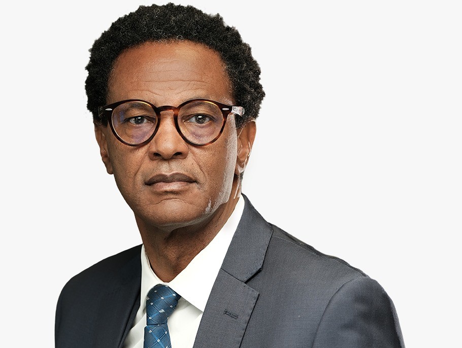 Professional man in a dark gray suit and blue tie, wearing round glasses, looking straight at the camera.