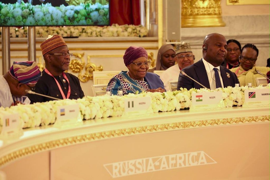 Delegates seated at a formal Russia–Africa conference table with microphones, floral garlands, and country nameplates.