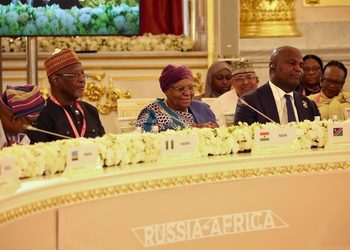Delegates seated at a formal Russia–Africa conference table with microphones, floral garlands, and country nameplates.